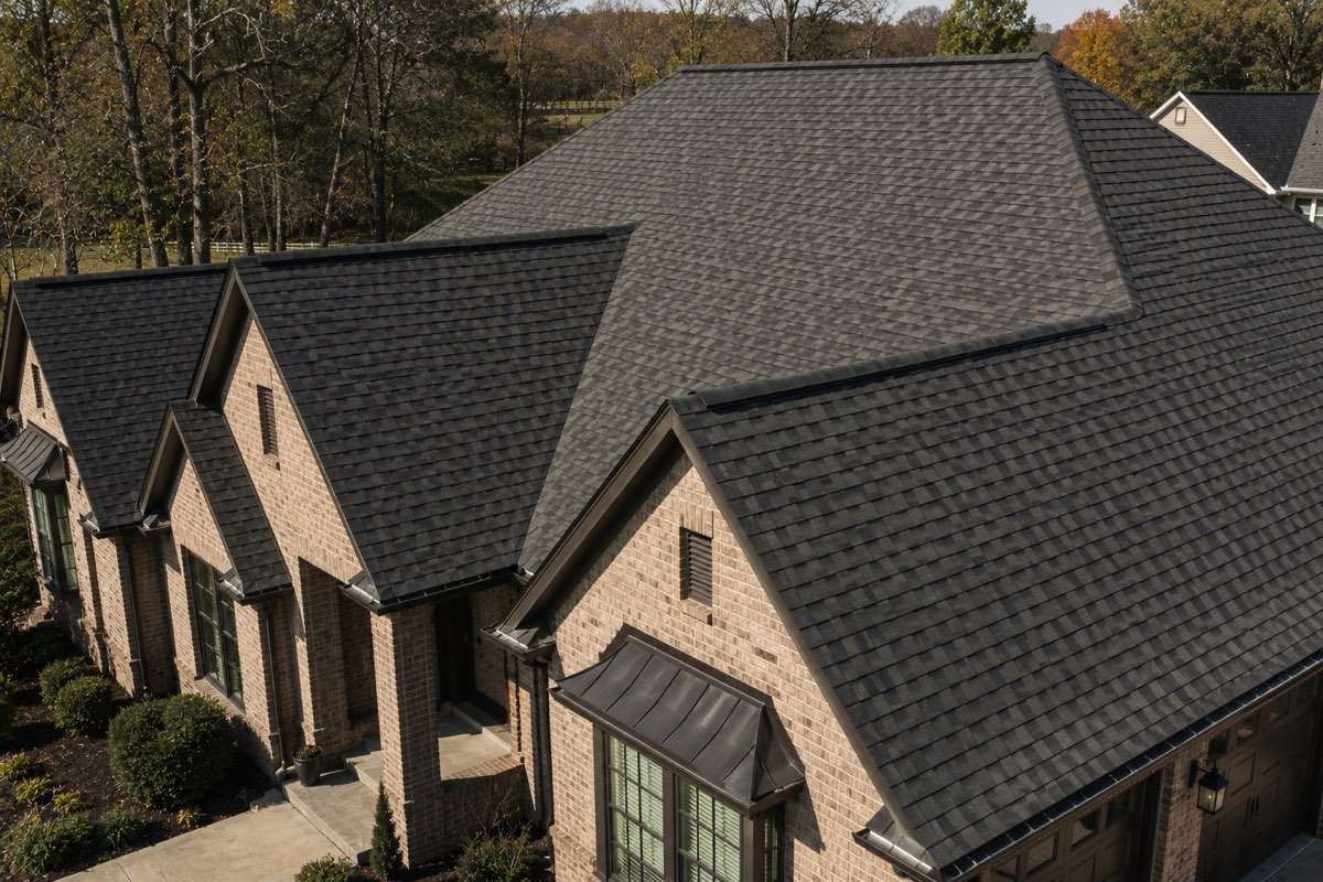 Aerial view of a finished architectural shingle roof on a brick home, showing the gables, valleys and new metal accent roofing