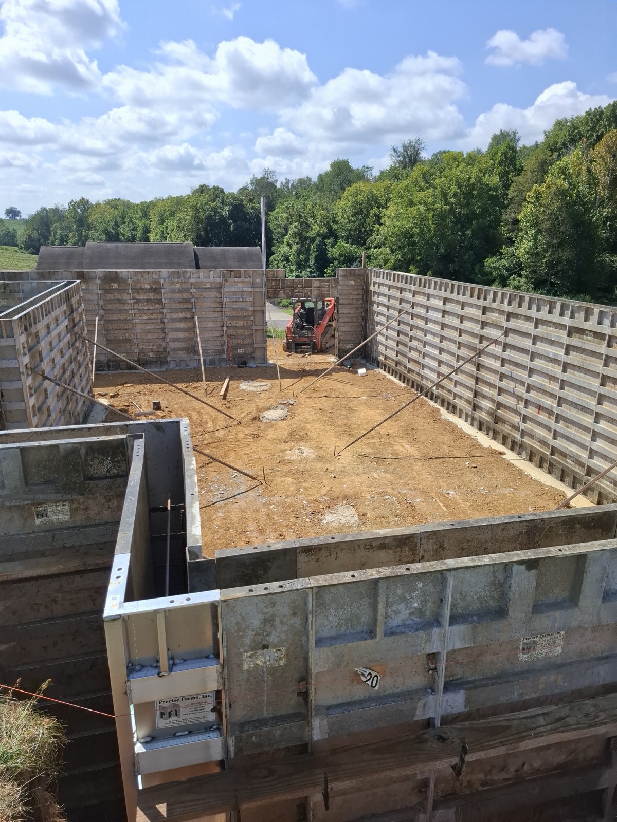 Concrete form walls enclosing a full house foundation footprint, with a skid steer grading the floor inside
