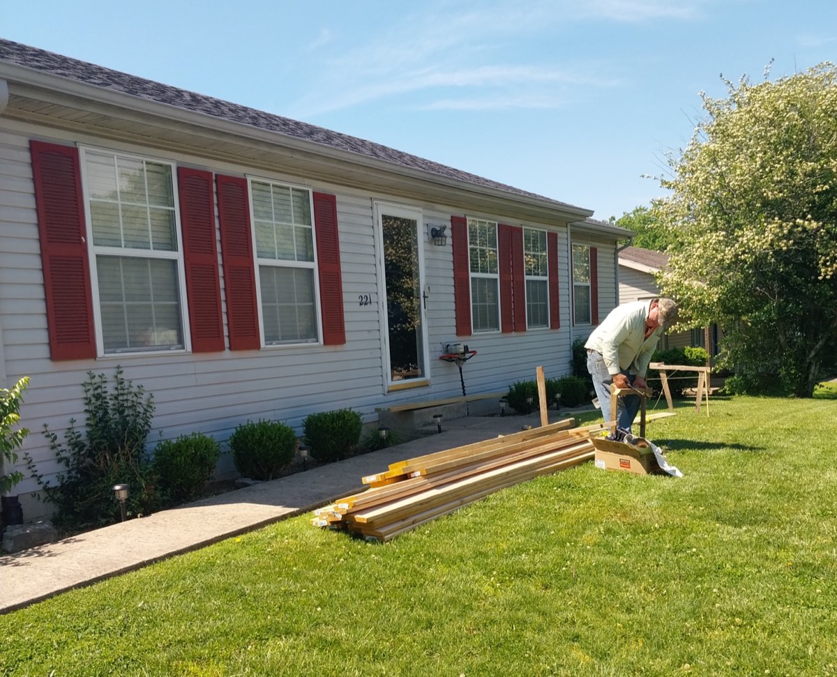 Ranch home in Danville with porch lumber stacked on the lawn before construction, red shutters and a bare front entry